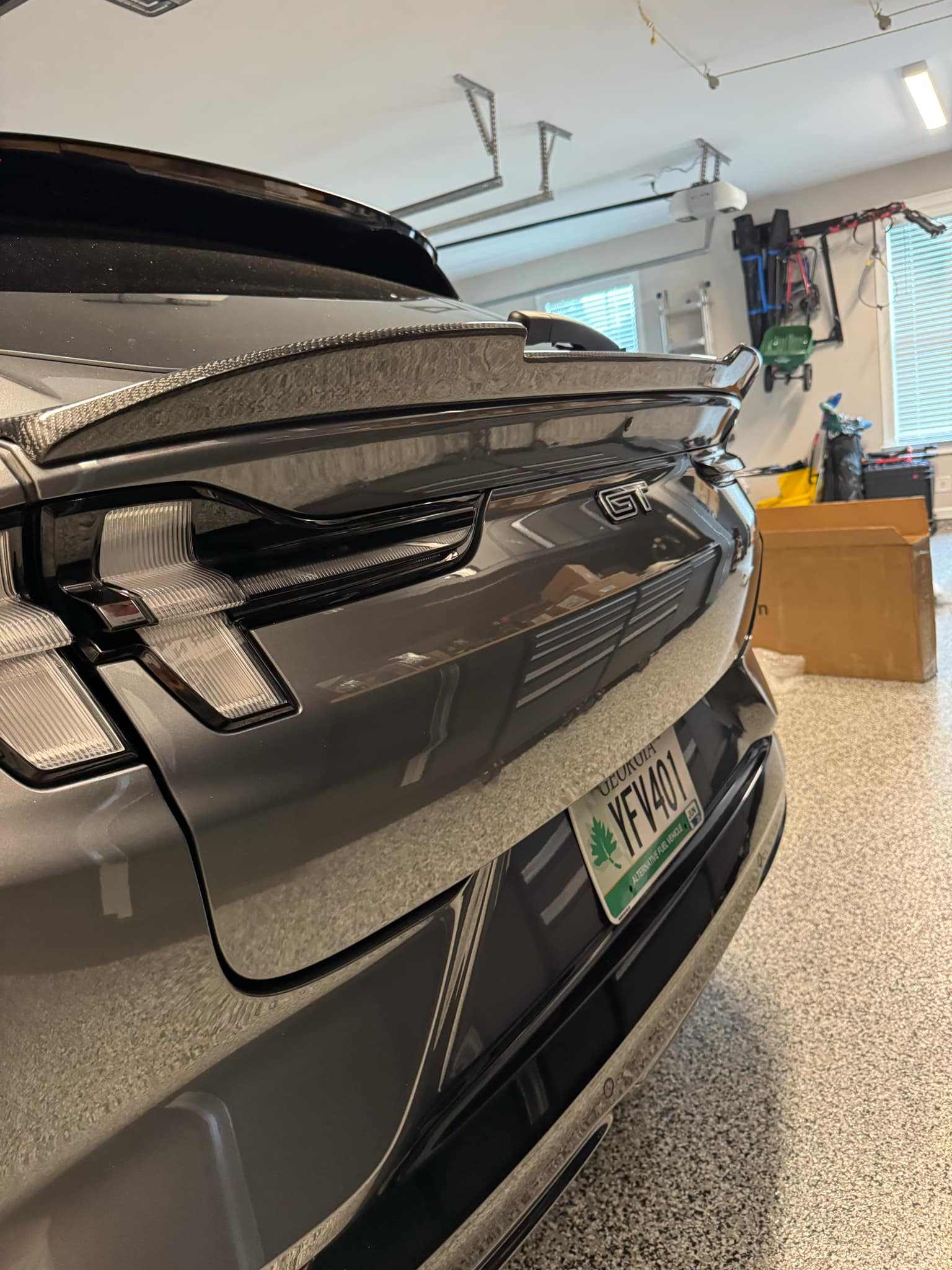 Wet carbon fiber Spoiler V2 installed on rear of gray Mustang Mach-E GT in garage