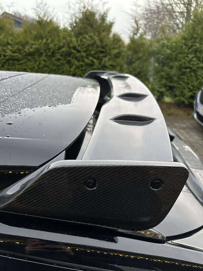 Close-up of a carbon fiber Rally Wing Spoiler installed on a black Ford Mustang Mach-E, showcasing its aerodynamic design and glossy finish with raindrops on the surface.