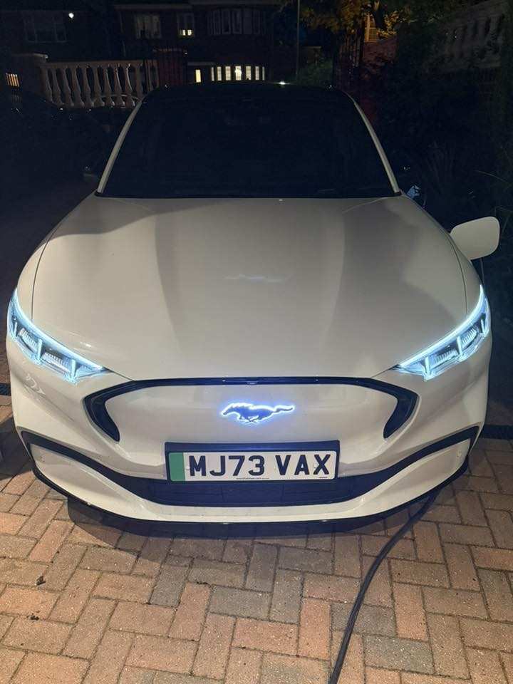 White Mustang Mach-E front view with illuminated blue Light-Up Pony emblem at night